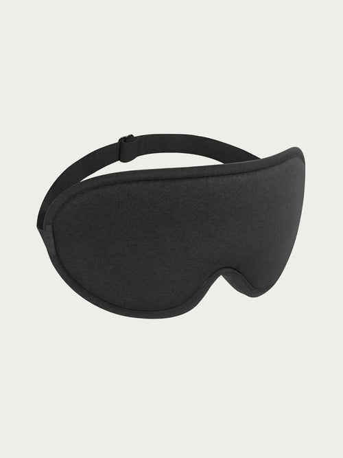 A black sleep mask with a curved design and adjustable strap is centered against a light gray background, conveying comfort and relaxation.