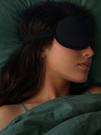 Woman sleeping with a black sleep mask on a green pillow