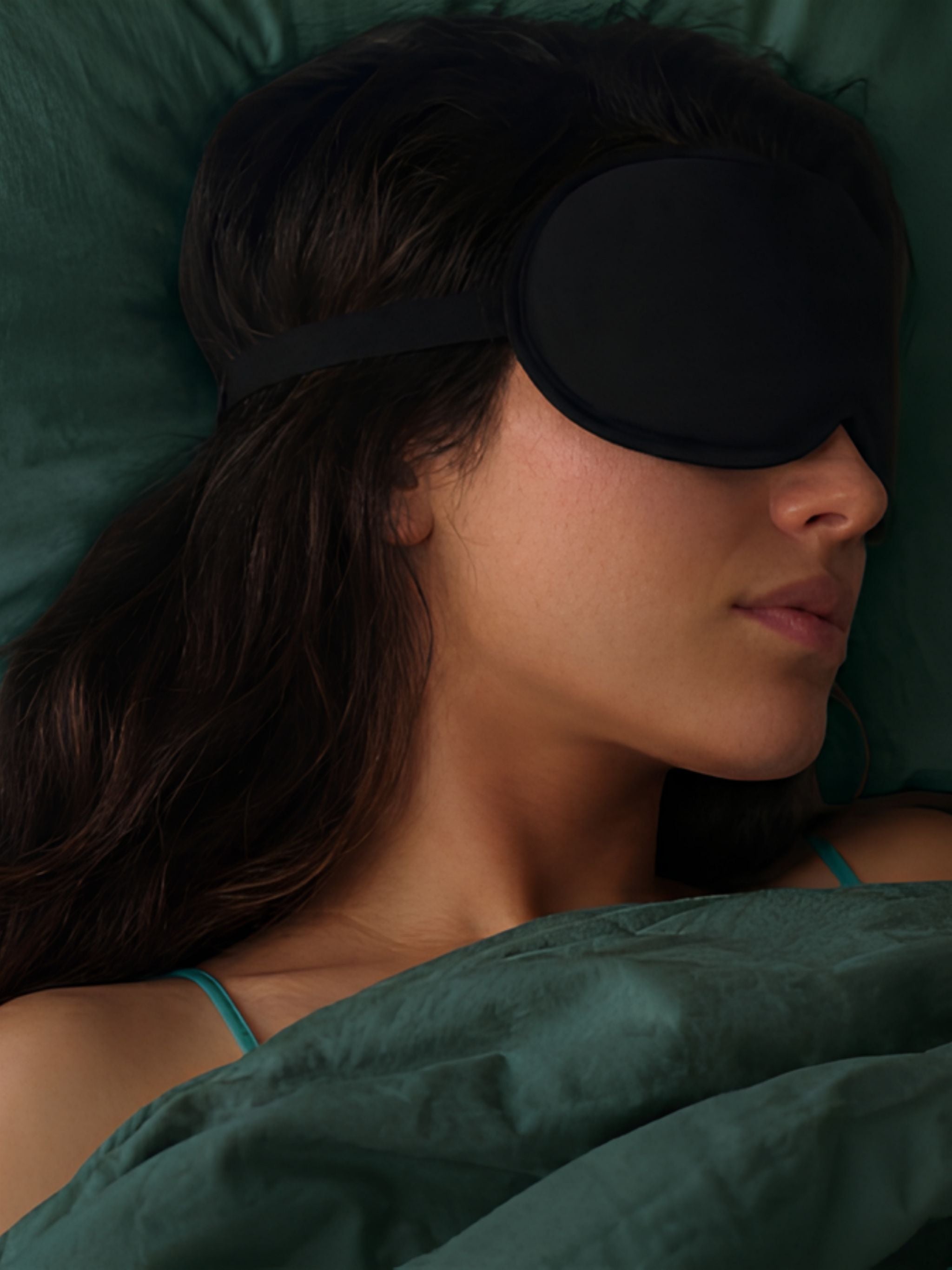 Woman sleeping with a black sleep mask on a green pillow