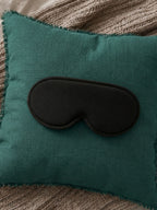 Teal pillow with a black eye mask on a textured surface