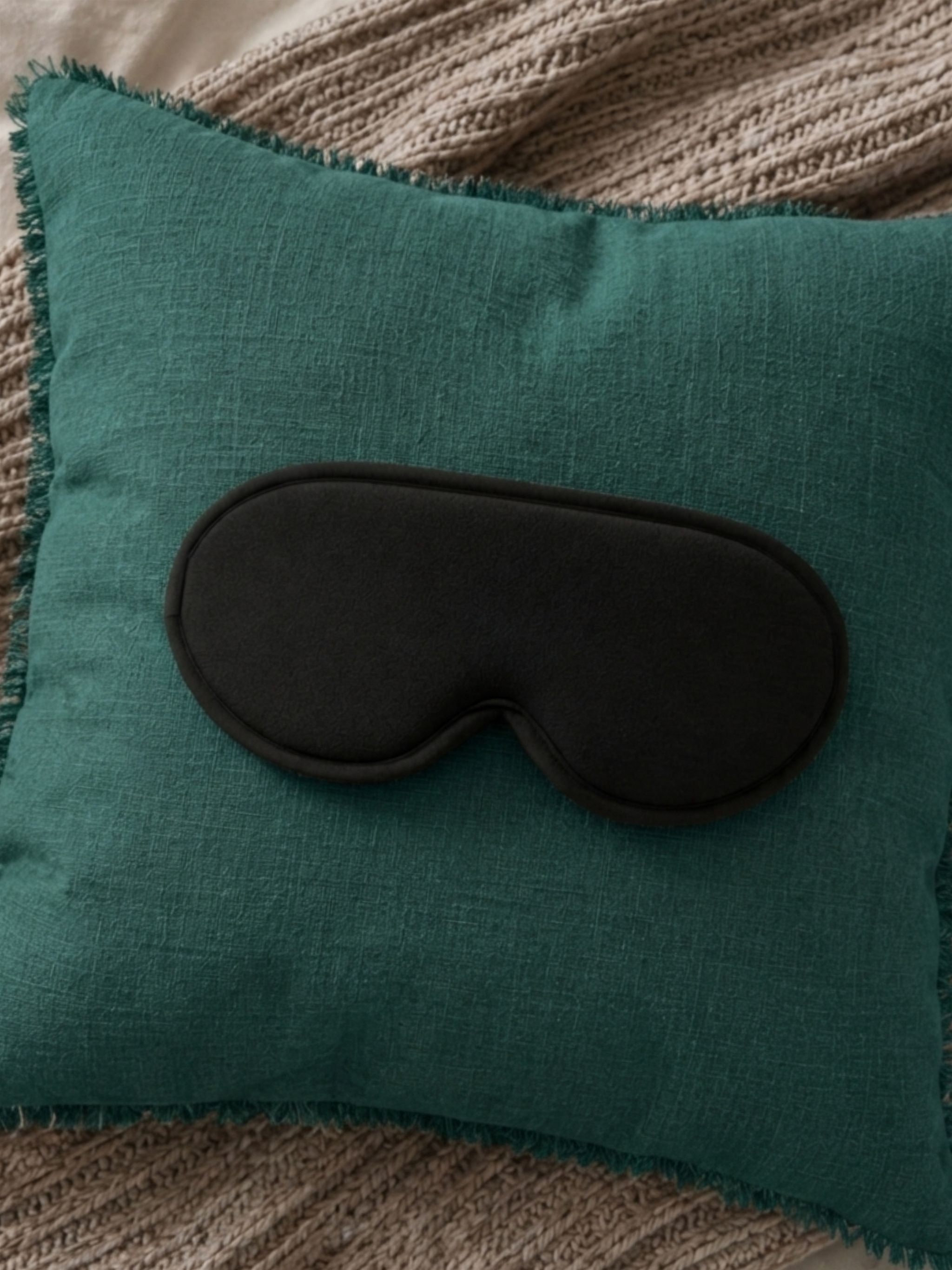 Teal pillow with a black eye mask on a textured surface